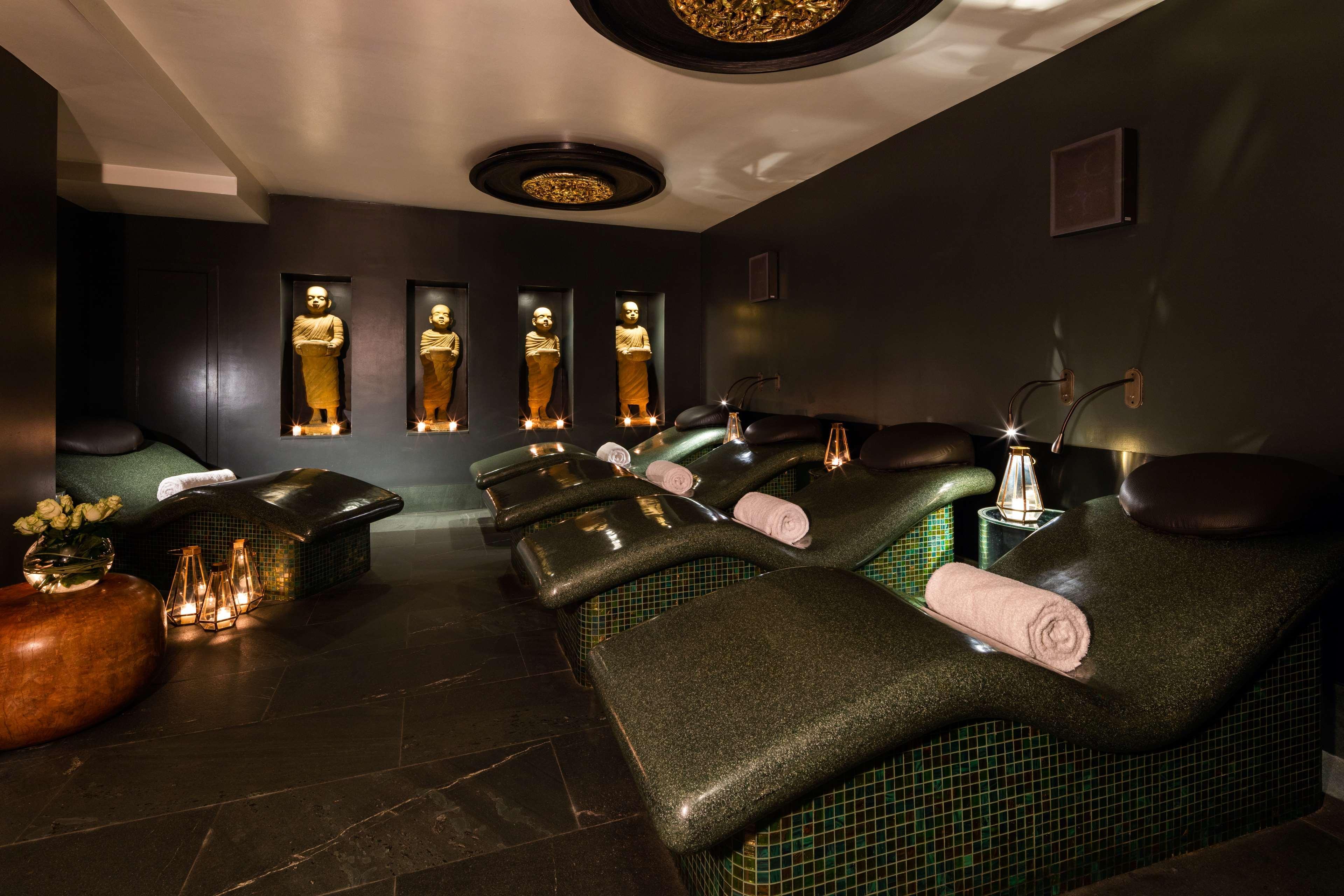 The May Fair, A Radisson Collection Hotel, Mayfair London Exterior photo The photo shows a tranquil spa environment. It features lounge chairs with curved backs, designed for relaxation, positioned in a dimly lit room. The walls are decorated in dark tones, providing a calming atmosphere. There are illuminated statues or 