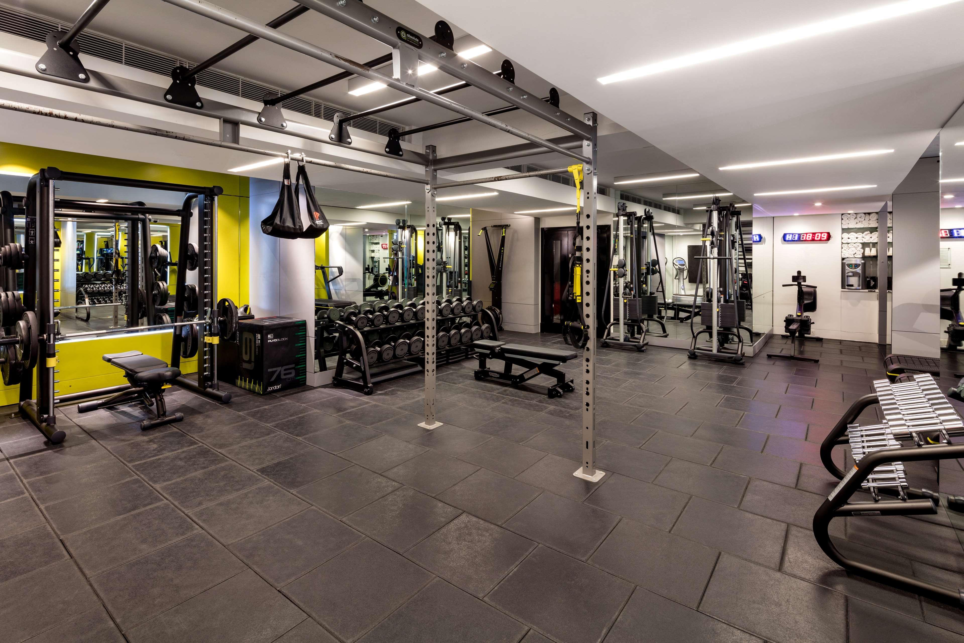 The May Fair, A Radisson Collection Hotel, Mayfair London Exterior photo The photo shows a modern gym interior. It features various workout equipment, including free weights, weight benches, and a cable machine. The space is well-lit, with a bright yellow accent wall. There are also functional training items like suspensi