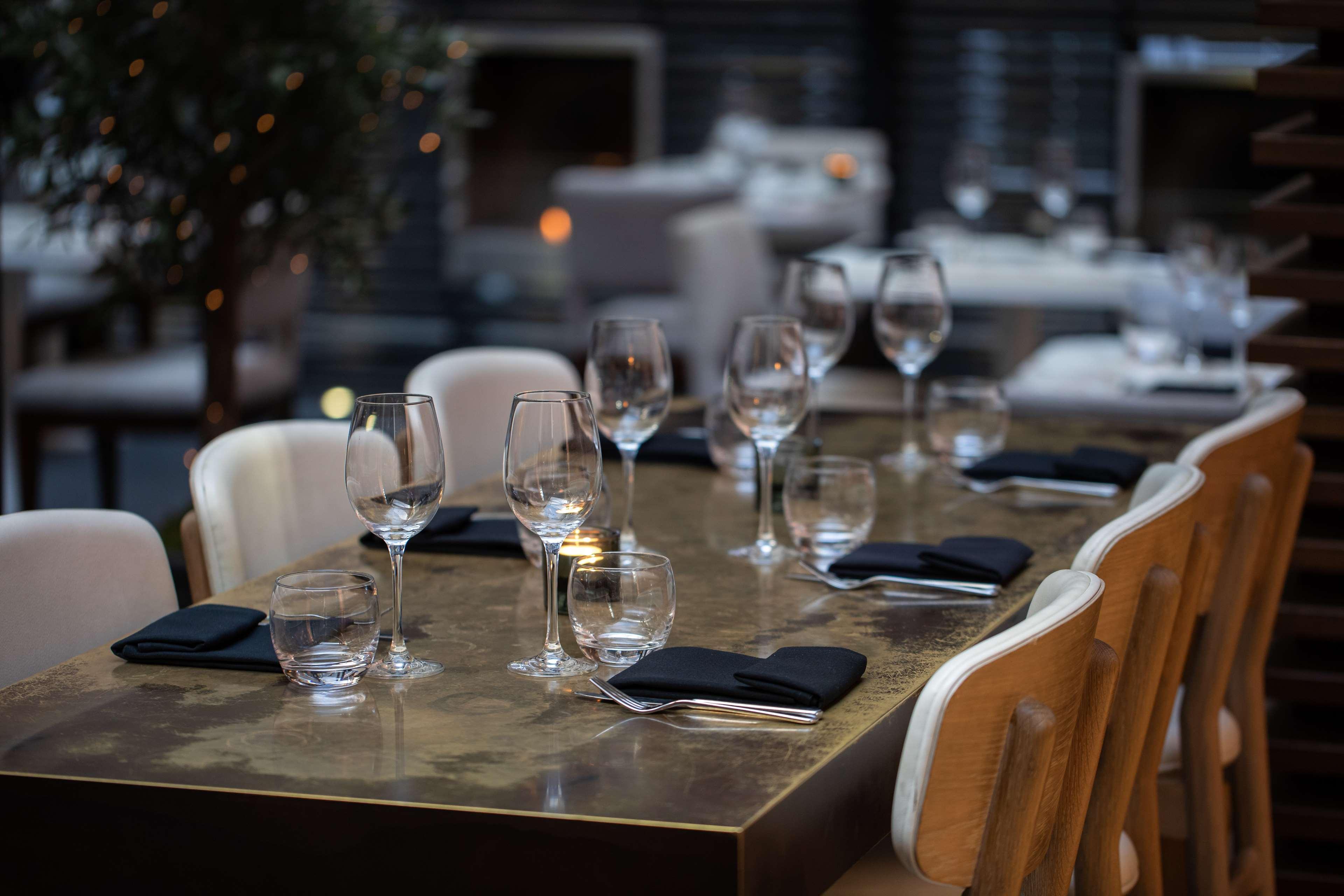 The May Fair, A Radisson Collection Hotel, Mayfair London Exterior photo The photo shows a dining table set for a meal. The table is made of a dark, polished material and has several place settings. Each setting features a wine glass, a smaller glass, and a neatly folded black napkin. The atmosphere appears elegant, with 