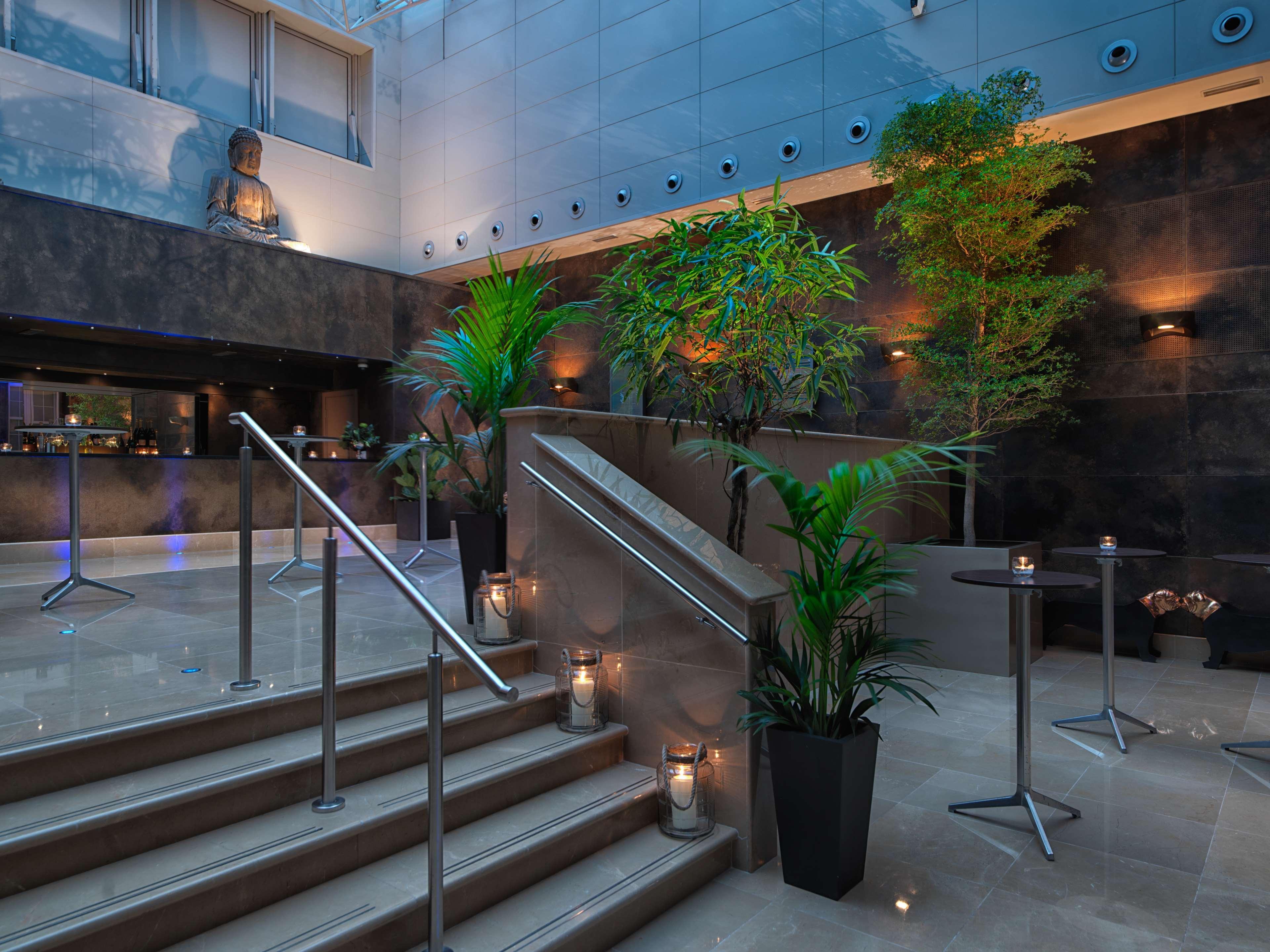 The May Fair, A Radisson Collection Hotel, Mayfair London Exterior photo The photo depicts a modern interior space, likely from a hotel or upscale venue. There is a stylish staircase leading upwards, flanked by decorative plants that add a touch of greenery to the environment. Soft lighting highlights the design elements,